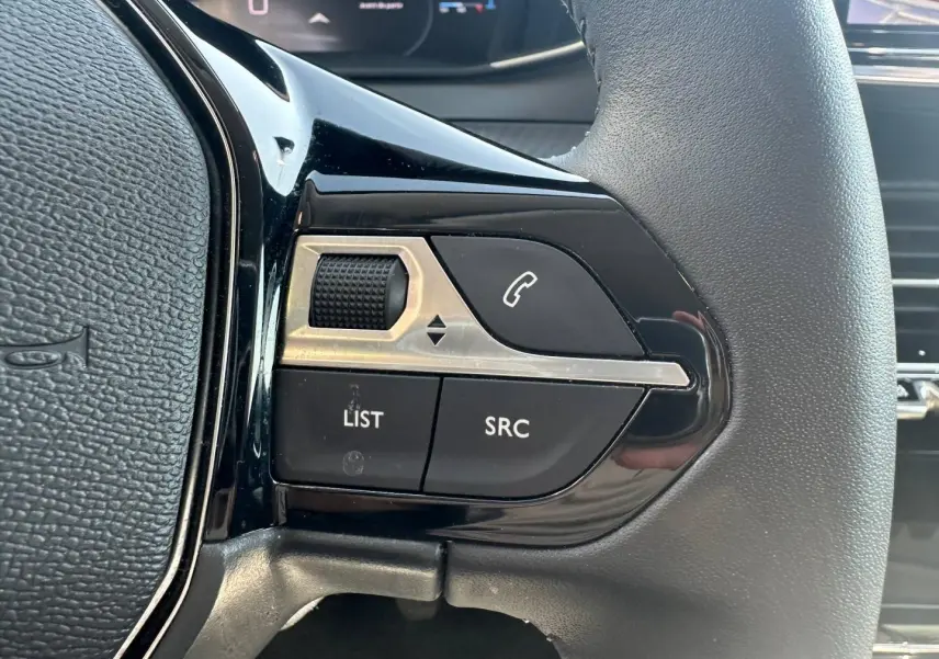 Gros plan sur les commandes gauche du volant noir de la Peugeot 208 2025, boutons appel et réglage audio visibles.