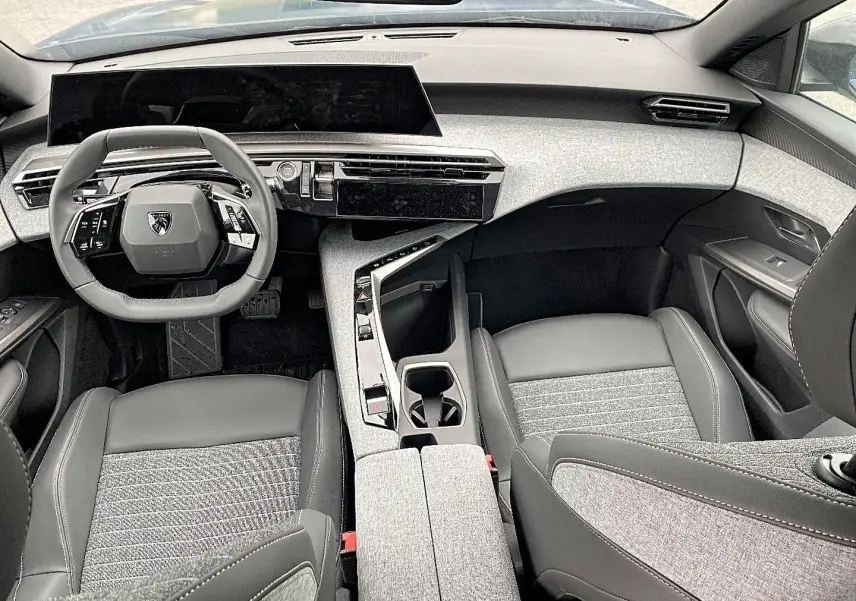 Vue intérieure avant du Peugeot 3008 bleu 2025, mettant en valeur le tableau de bord moderne et les sièges bi-matière gris et noir.