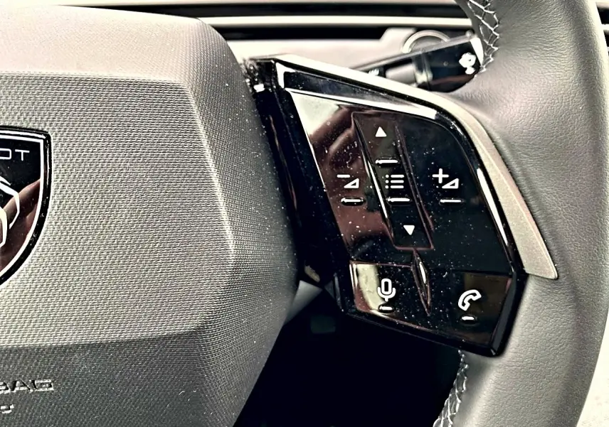 Gros plan sur le volant cuir noir de la Peugeot 3008 2025, avec commandes multifonctions et logo central visible.
