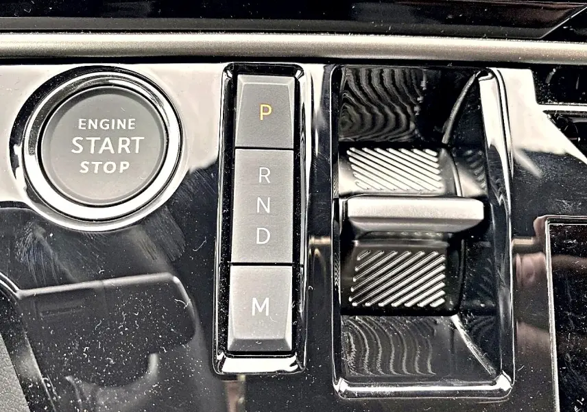 Gros plan sur la console centrale noire brillante du Peugeot 3008 1.2 hybrid 145 allure e-dcs6 avec bouton start/stop et sélecteur de boîte auto.