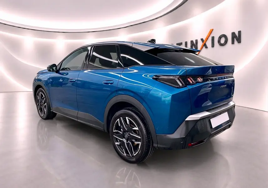Vue 3/4 arrière droite du Peugeot 3008 bleu 2025 avec jantes alliage et toit noir brillant dans un showroom lumineux.