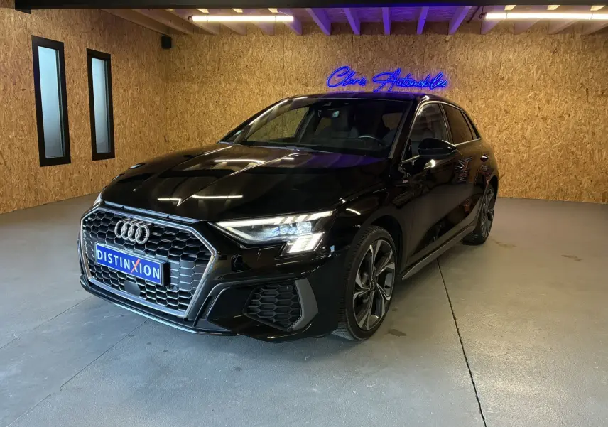 Audi A3 Sportback noir vue 3/4 avant droit en intérieur, avec calandre hexagonale et phares LED allumés.