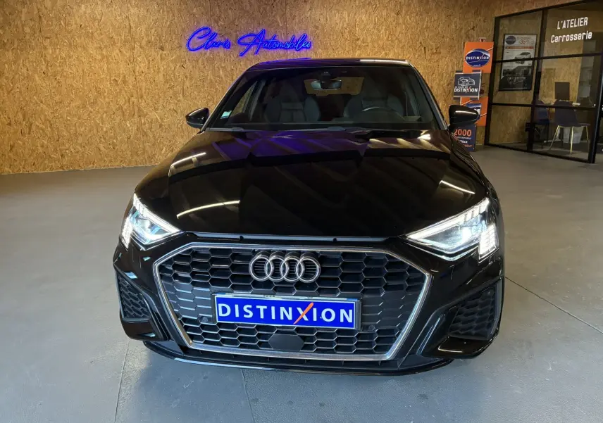Vue frontale d'une Audi A3 Sportback noire 2022 avec calandre hexagonale et phares LED allumés en intérieur showroom.