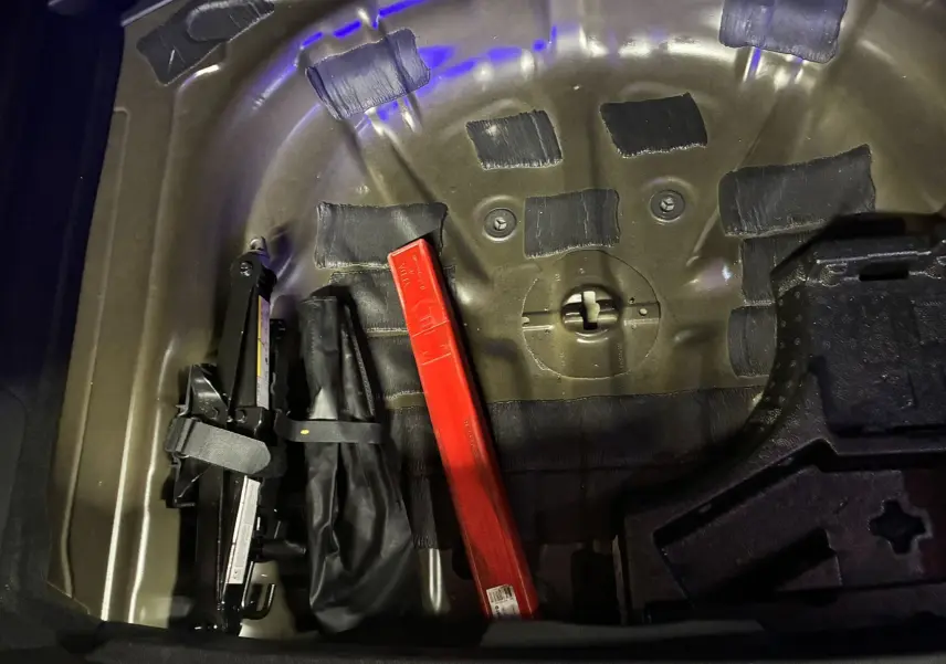 Vue rapprochée du coffre d'une Audi A3 Sportback 2022, montrant le rangement sous le plancher avec un cric et un triangle de signalisation rouge.