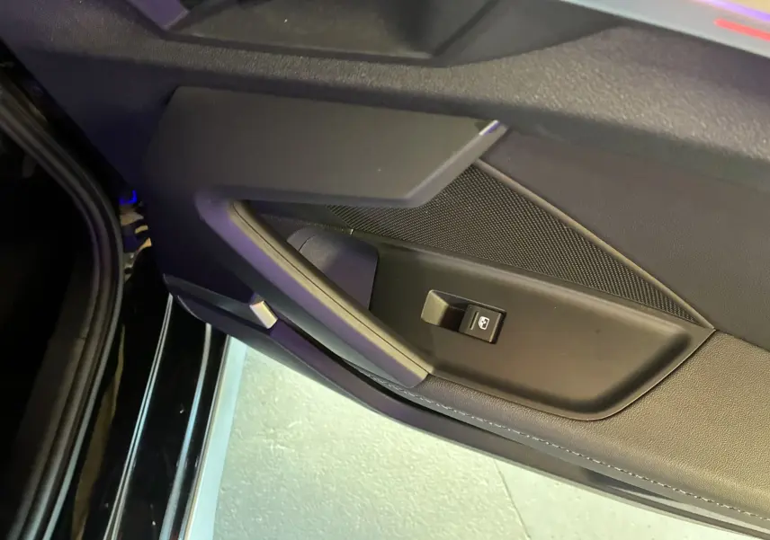 Gros plan sur la poignée intérieure et le bouton de lève-vitre côté gauche d'une Audi A3 Sportback noire de 2022.