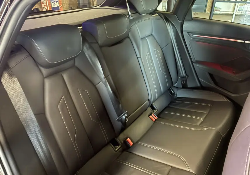Vue intérieure du siège arrière en cuir noir de l'Audi A3 Sportback 2022, avec surpiqûres blanches et ceintures visibles.