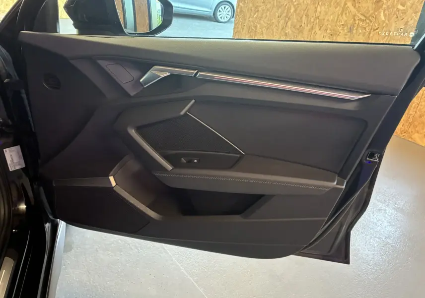Vue intérieure côté gauche de la porte noire de l'Audi A3 Sportback 2022 avec garniture sobre et éléments métalliques.