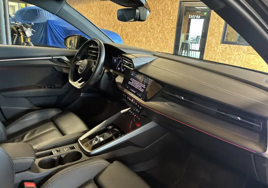 Intérieur noir de l'Audi A3 Sportback 2022, vue côté conducteur, tableau de bord moderne avec écran tactile et volant cuir.