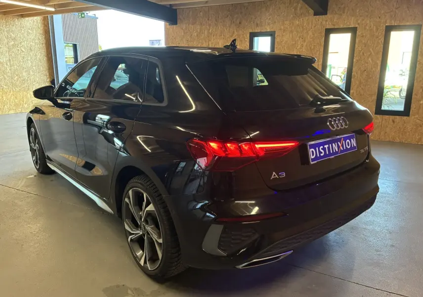 Audi A3 Sportback noir vue en 3/4 arrière droit dans un garage avec feux arrière allumés et jantes S Line.