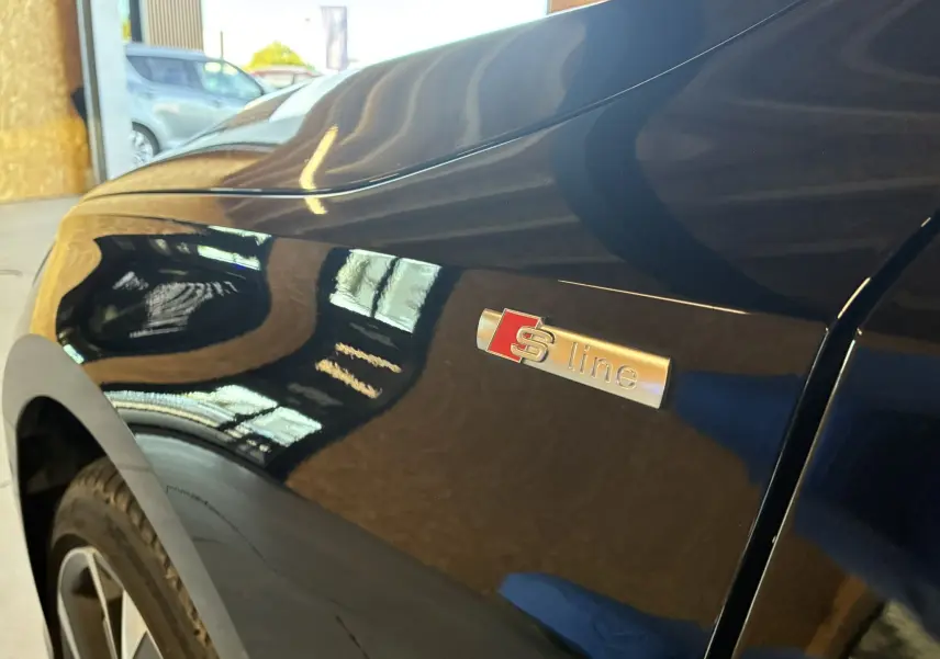 Gros plan sur l'aile avant côté gauche d'une Audi A3 Sportback noire avec le badge S line brillant.