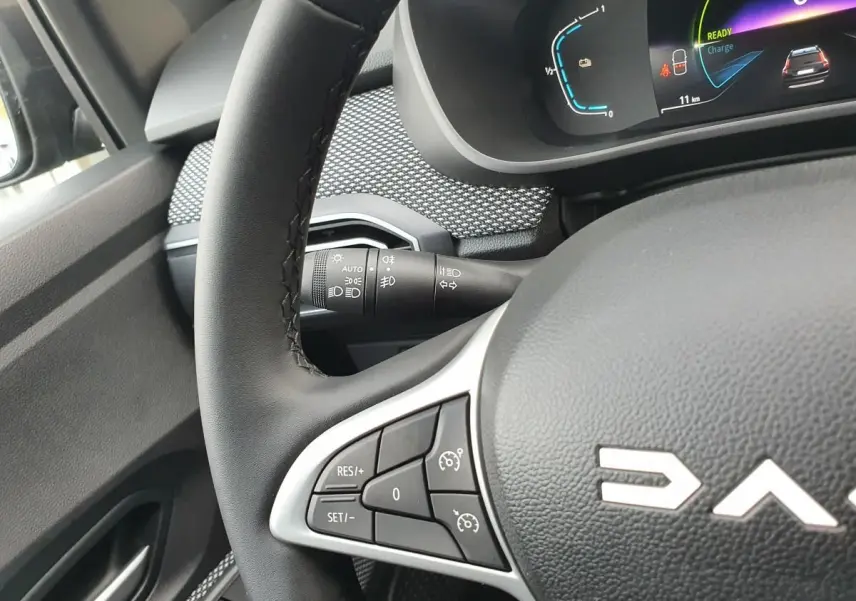 Gros plan sur le volant noir de la Dacia Jogger 2024 avec commandes intégrées et tableau de bord numérique partiellement visible.