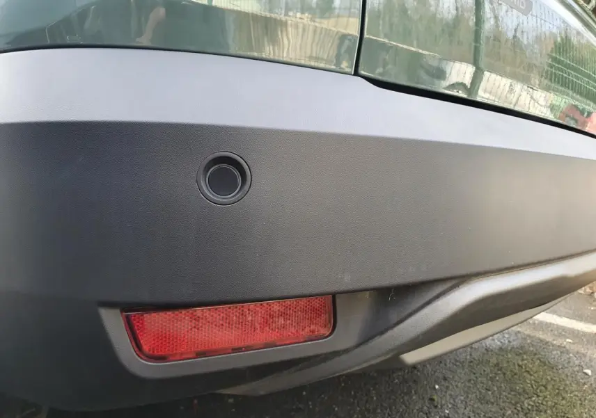 Gros plan sur le pare-chocs arrière kaki métallisé du Dacia Jogger 1.6 Hybrid avec capteur de recul et feu antibrouillard.