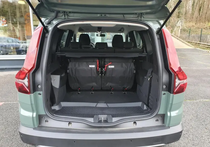Vue arrière ouverte du Dacia Jogger 2024 en Licken Kaki, montrant le coffre spacieux avec banquette rabattue et feux arrière rouges.