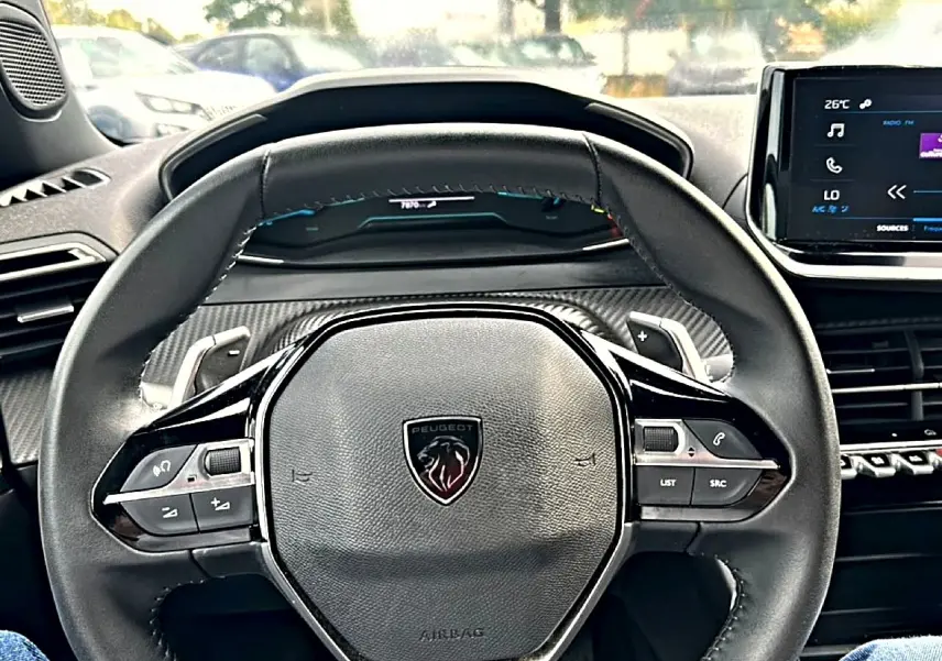 Vue centrée sur le volant cuir noir du Peugeot 2008 gris, avec commandes intégrées et tableau de bord numérique.