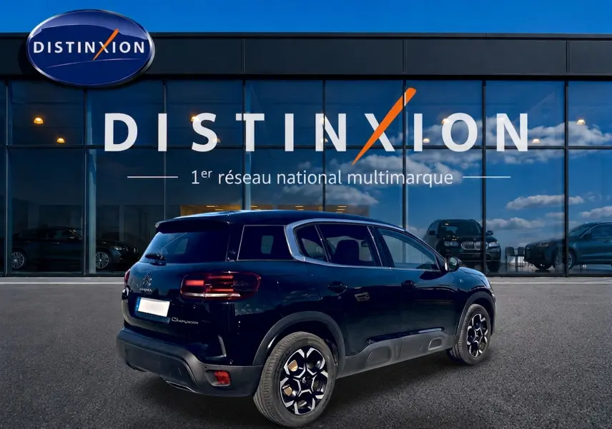 Vue 3/4 arrière droite d'un Citroën C5 Aircross noir 2024 avec jantes alu et barres de toit devant un showroom Distinxion.