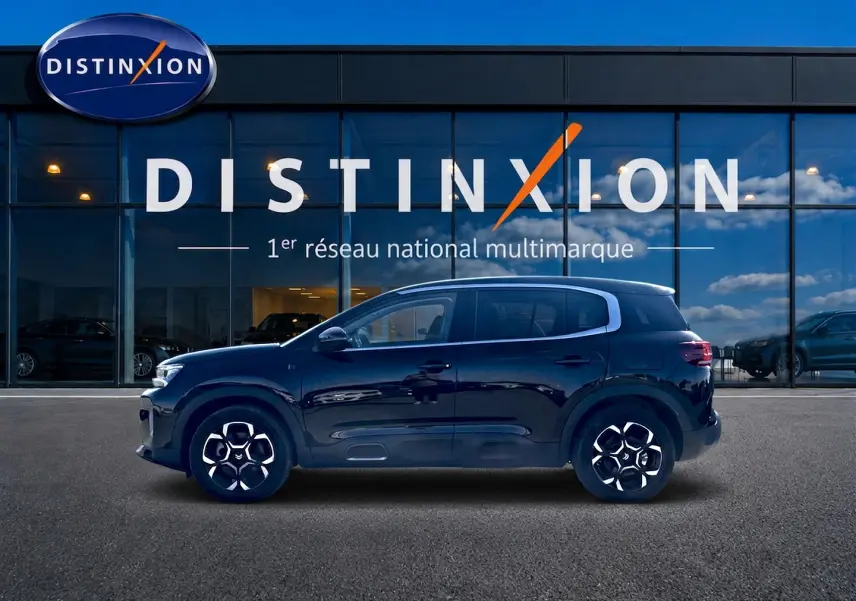 Profil côté gauche d'un Citroën C5 Aircross noir 2024 devant une vitrine avec logo Distinxion.
