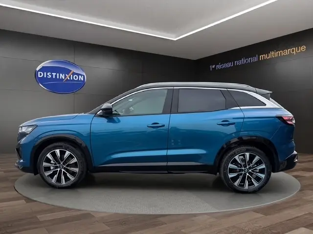 Profil latéral droit du Renault Austral bleu bi-ton avec jantes alliage et toit blanc dans un showroom.