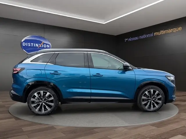 Profil droit du Renault Austral 2026 bleu bi-ton avec toit noir et jantes alliage distinctives en exposition intérieure.