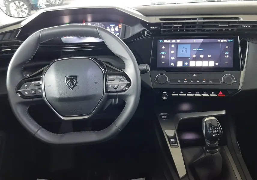 Vue intérieure frontale du tableau de bord noir de la Peugeot 308 2022 avec volant compact et écran tactile central.