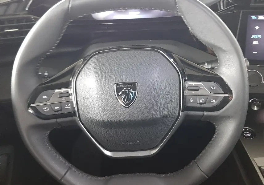 Gros plan sur le volant cuir noir de la Peugeot 308 2022, affichant le logo lion au centre et commandes intégrées.