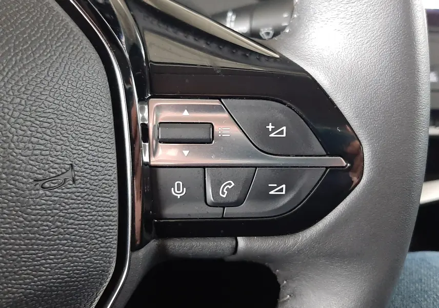 Gros plan sur les commandes multifonctions à gauche du volant en cuir noir de la Peugeot 308 blanche.