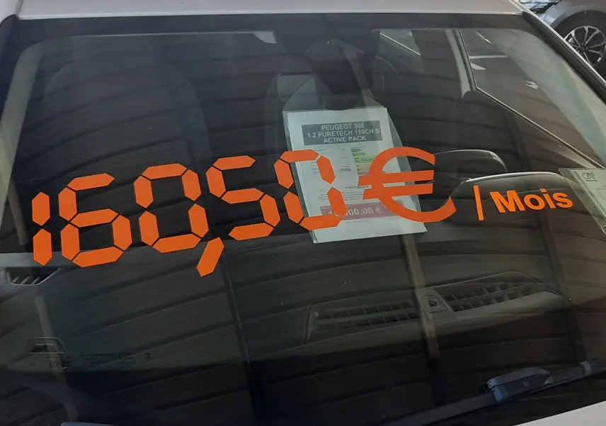 Vue avant rapprochée d'une Peugeot 308 blanche avec affichage orange du prix mensuel sur le pare-brise.