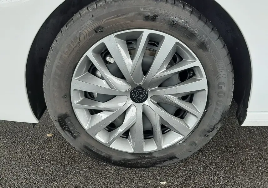 Gros plan sur la roue avant droite d'une Peugeot 308 blanche avec jante alliage argentée et logo Peugeot central.