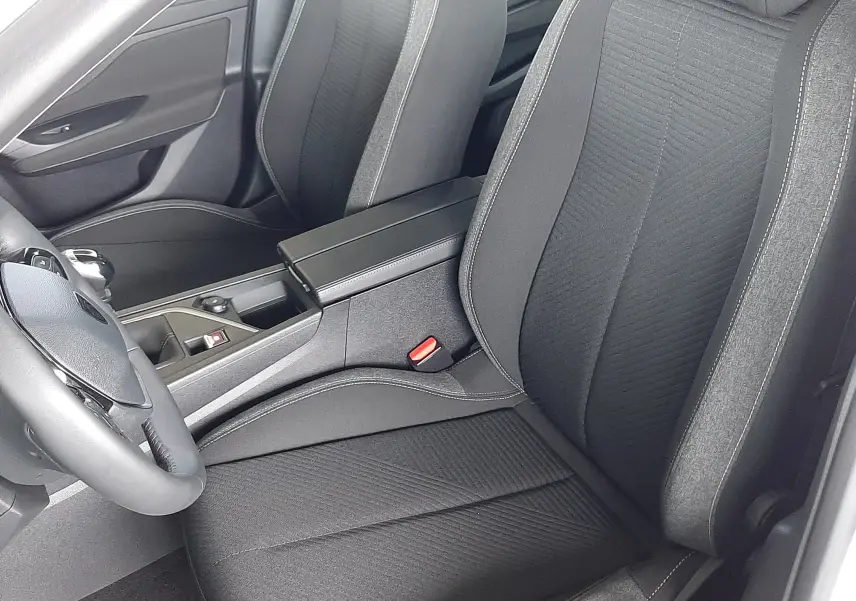 Vue intérieure côté conducteur de la Peugeot 308 2022 avec sièges tissu noir et accoudoir central.