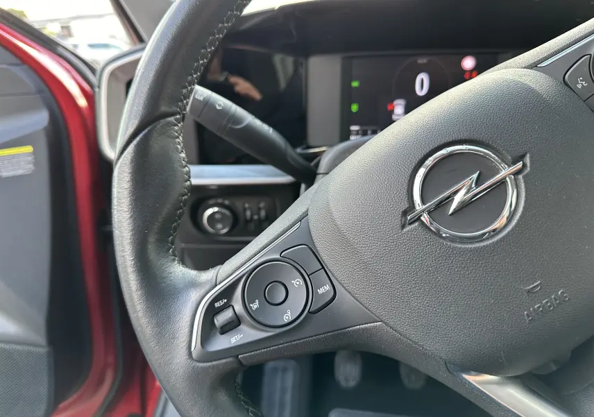 Gros plan sur le volant noir d'une Opel Mokka rouge Kardinal 2021, montrant les commandes au volant côté gauche.