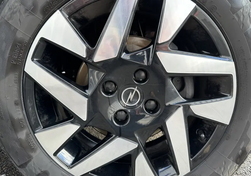 Gros plan sur la jante en alliage bicolore noir et argent avec logo Opel au centre du SUV Mokka rouge Kardinal.