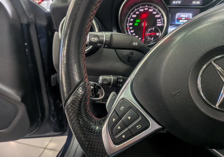 Vue rapprochée du volant cuir noir avec commandes intégrées et tableau de bord éclairé d'une Mercedes Classe CLA 2017.