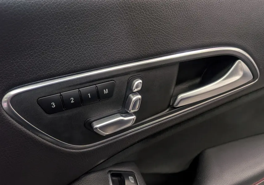 Gros plan sur la commande de réglage électrique des sièges côté gauche en cuir noir de la Mercedes CLA 200 Fascination.