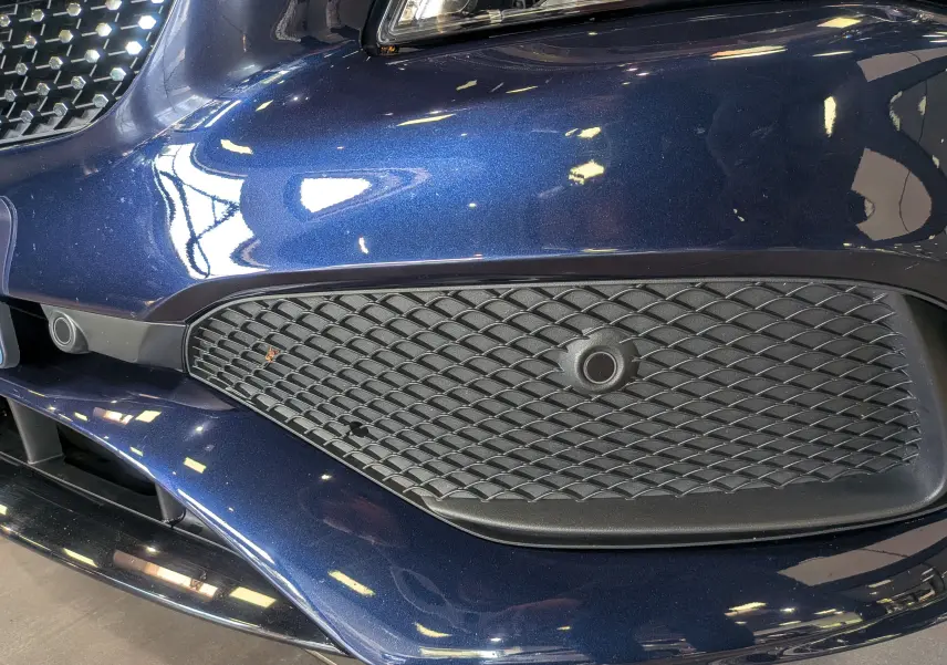 Gros plan sur la calandre avant droite bleu Cavansite d'une Mercedes CLA 200 Fascination 2017 avec capteur de stationnement intégré.