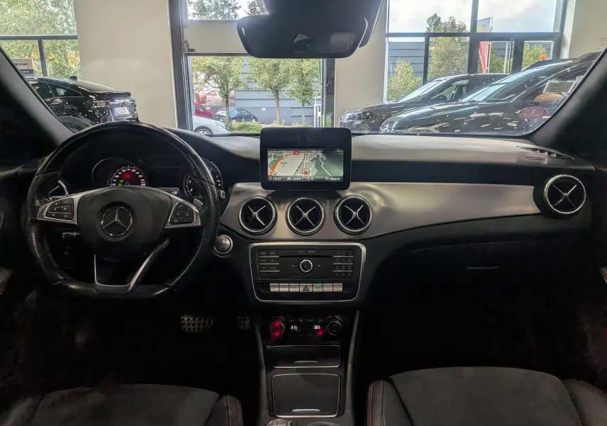 Vue intérieure avant du tableau de bord d'une Mercedes Classe CLA 200 Fascination 2017 avec écran GPS et aérateurs ronds chromés.