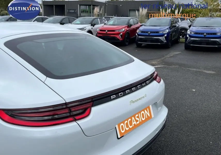 Vue arrière droite d'une Porsche Panamera 4 E-Hybrid blanche avec feux LED et logo Porsche bien visibles.