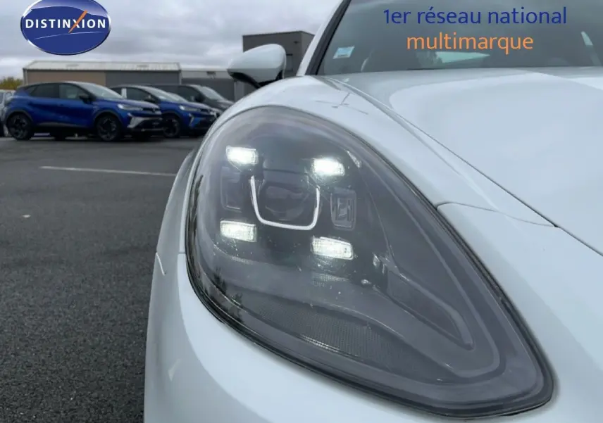 Gros plan sur le phare avant gauche allumé d'une Porsche Panamera 4 E-Hybrid blanche de 2017.