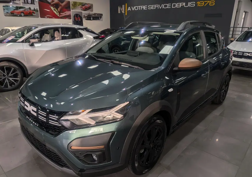 Vue 3/4 avant droite d'une Dacia Sandero Stepway TCe 110 Vert Cèdre avec rétroviseurs marron en showroom.