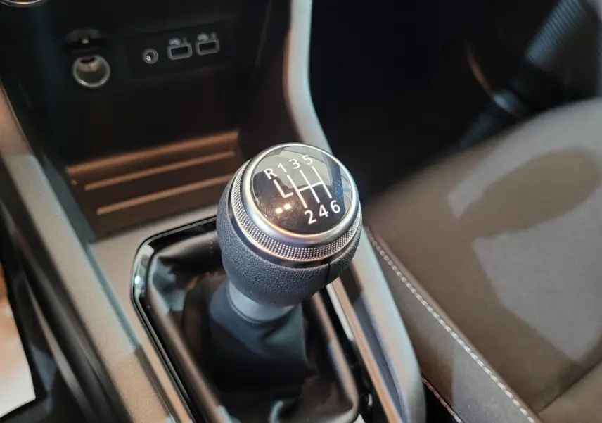 Gros plan sur le levier de vitesses manuel de la Renault Clio gris foncé, avec console centrale et siège tissu visible.