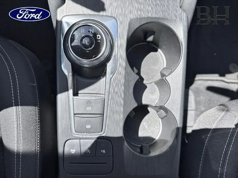 Vue plongeante sur la console centrale noire du Ford Kuga 2022 avec sélecteur rotatif de boîte auto et porte-gobelets.