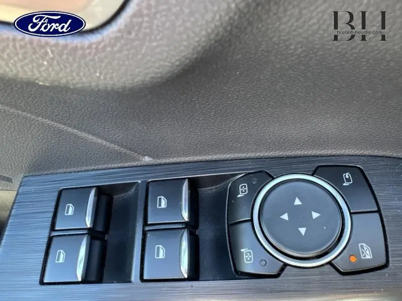 Gros plan sur les commandes de lève-vitres et réglage des rétroviseurs côté conducteur du Ford Kuga gris.