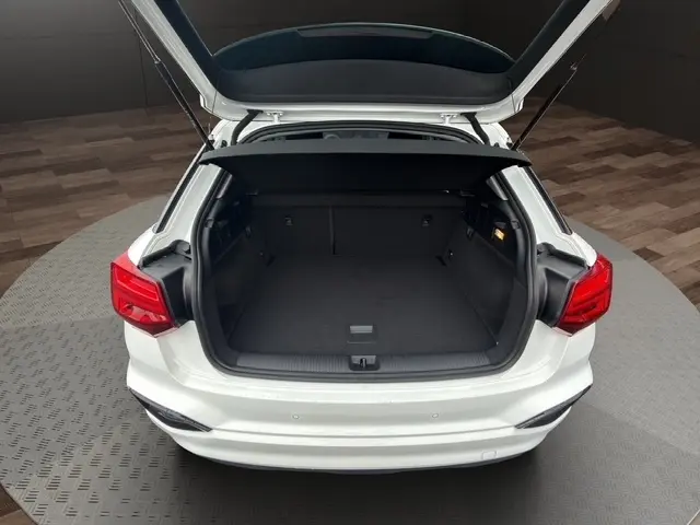 Vue arrière ouverte du coffre d'un Audi Q2 blanc 30 TDI 116 Design, avec banquette rabattable et feux arrière LED visibles.