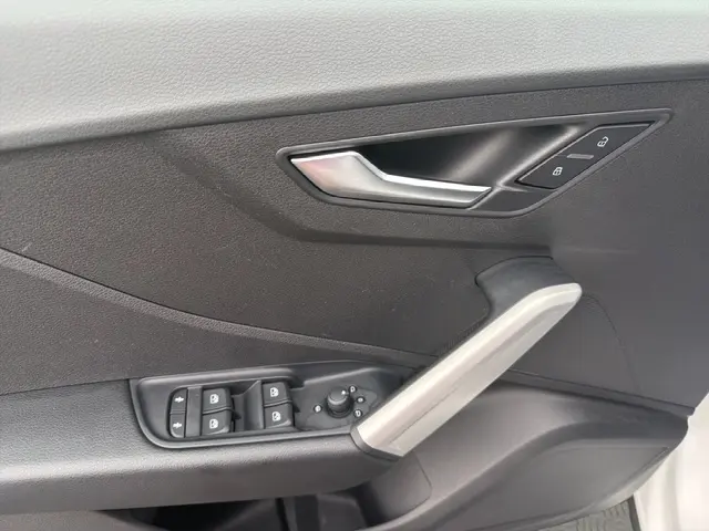 Vue rapprochée de la porte avant gauche de l'Audi Q2 blanc, montrant la poignée argentée et les commandes électriques des vitres.