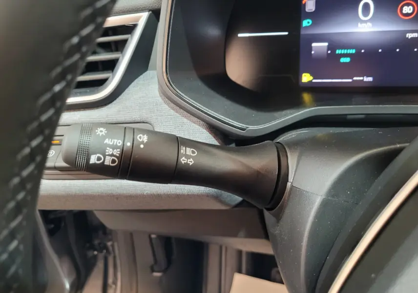 Gros plan sur la manette des phares à gauche du volant dans l'habitacle gris foncé de la Renault Clio 2025.