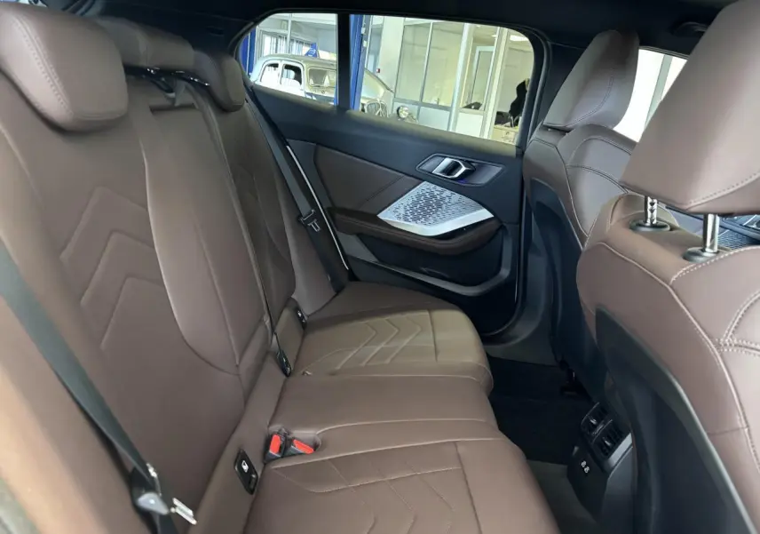 Vue intérieure arrière de la BMW Série 1 120d M Sport 2025, sièges en cuir marron et détails argentés sur les portes.