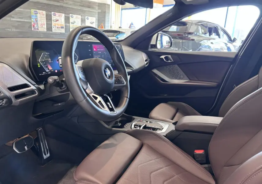 Vue intérieure côté conducteur de la BMW Série 1 120d M Sport 2025 avec tableau de bord numérique et sellerie marron.