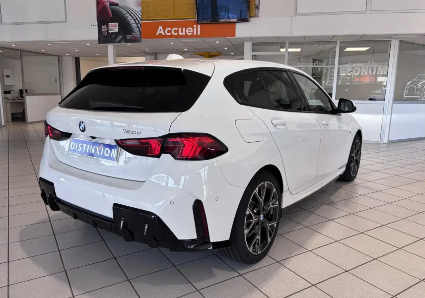 BMW Série 1 120d M Sport blanc vue 3/4 arrière droit en showroom, avec jantes noires et détails noirs contrastants.