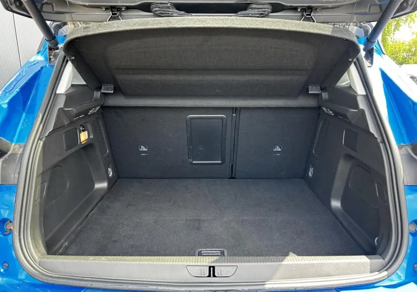 Coffre ouvert vu de l'arrière d'un Opel Grandland bleu Vertigo, espace de chargement vide et tapis noir.