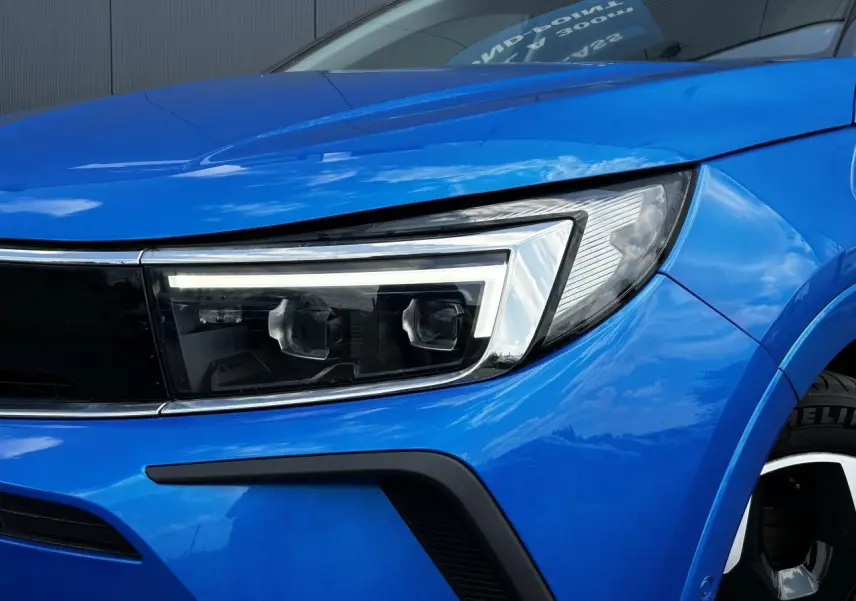 Gros plan sur le phare avant droit et la calandre d’un Opel Grandland bleu Vertigo avec jante alliage noire.
