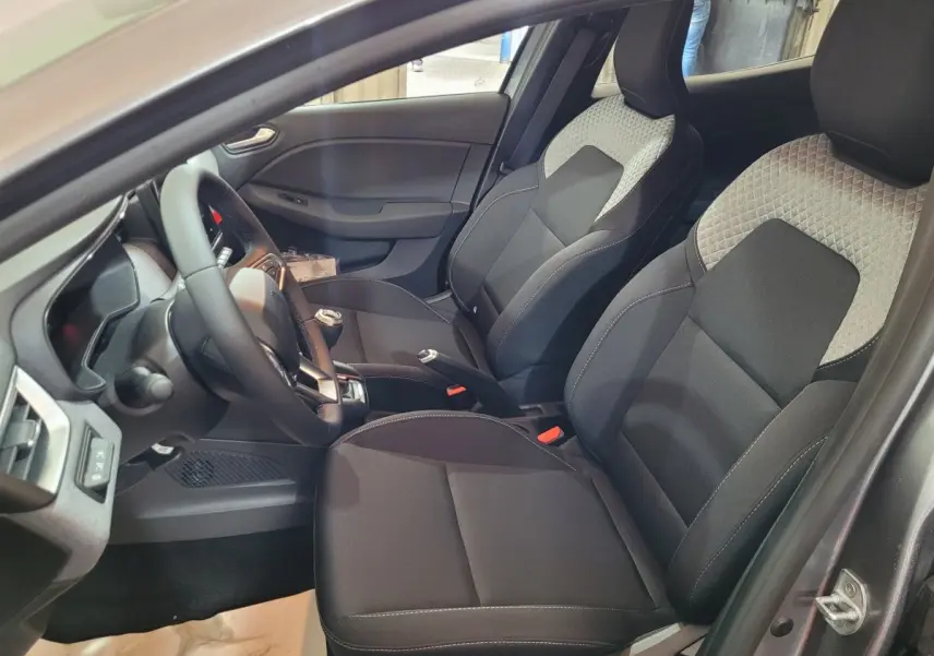 Vue intérieure côté conducteur de la Renault Clio 2025 gris foncé, sièges tissu noir avec inserts gris clair et volant multifonctions.