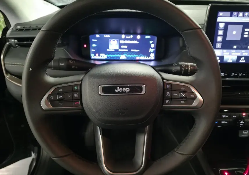 Vue rapprochée du volant noir Jeep Compass 2024 avec commandes intégrées et tableau de bord numérique en arrière-plan.